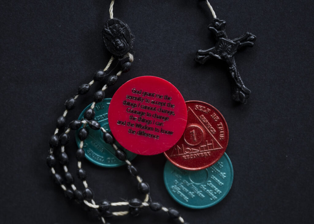 A photo of a rosary and sobriety chips
